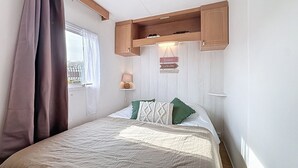 Een slaapkamer met een bed, een raam met gordijnen, een plank met een lamp en een bord aan de muur.
