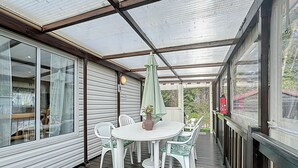 Een overdekt terras met een tafel en stoelen, een groene parasol en een brandblusser aan de rechterkant.