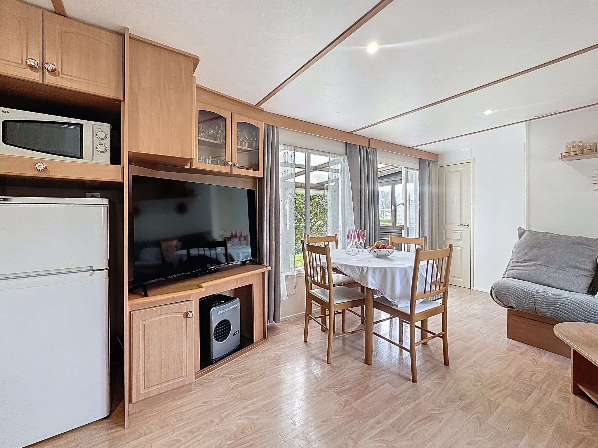 Een compacte keuken met een magnetron, koelkast en een inbouwoven. Er is een eethoek met een tafel en stoelen, en een bank in de woonkamer.