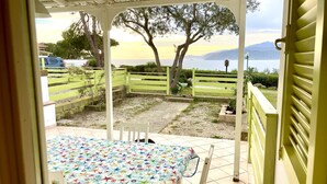Una veranda riparata con tavolo e sedie, vista mare e montagne, e un recinto verde.