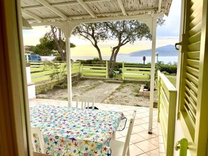 A covered patio with a table and chairs, a view of the sea and mountains, and a green fence. - Colibri 2 By ColombiElbaVacanze - Colibrì 2 (Capoliveri)