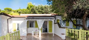 A white building with green shutters, a tiled patio, and a white fence. - Colibri 2 By ColombiElbaVacanze - Colibrì 2 (Capoliveri)