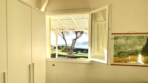 Una camera da letto con una finestra che si affaccia su un giardino e vista mare.