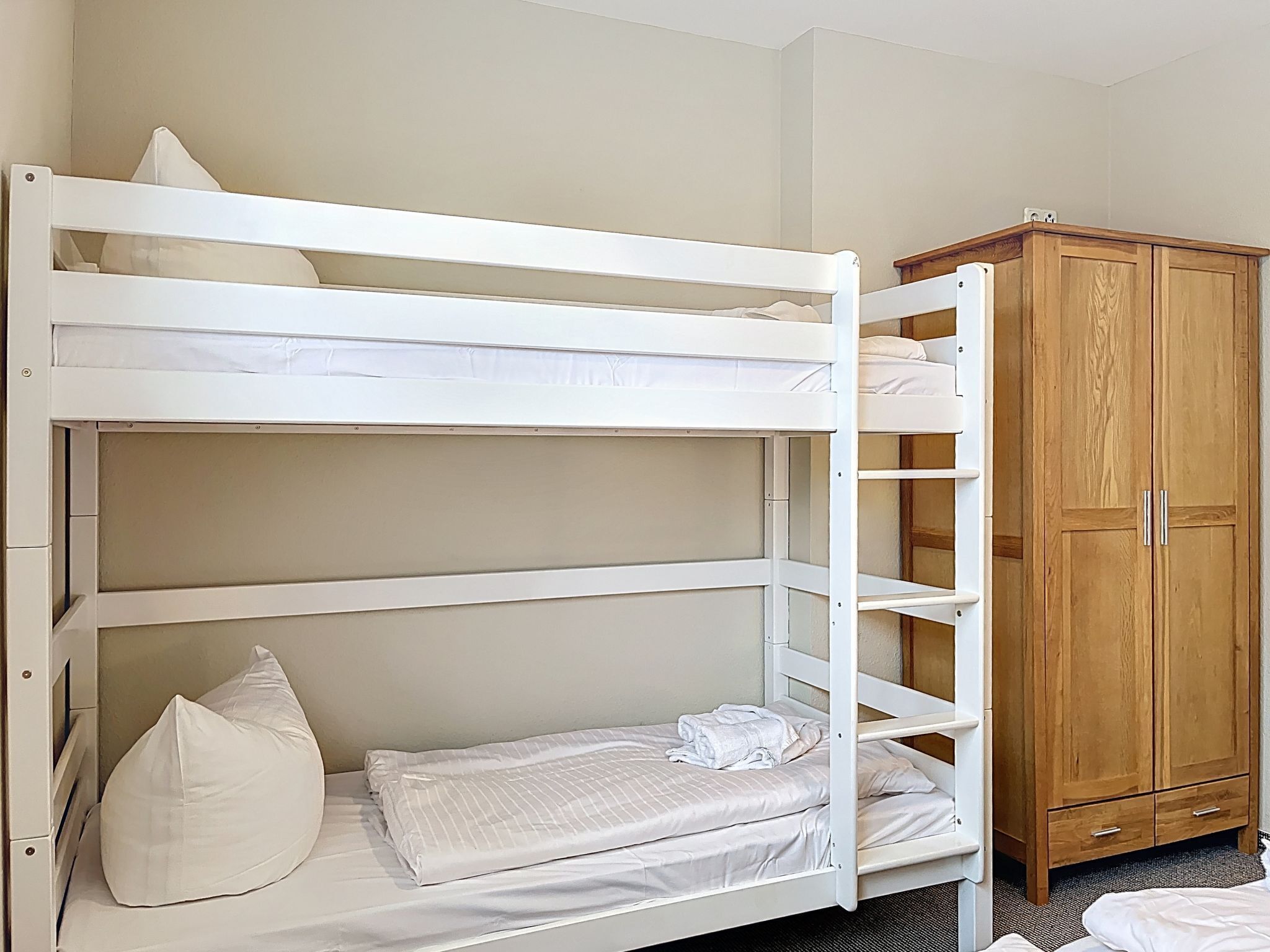 A bunk bed with white bedding and a wooden wardrobe.