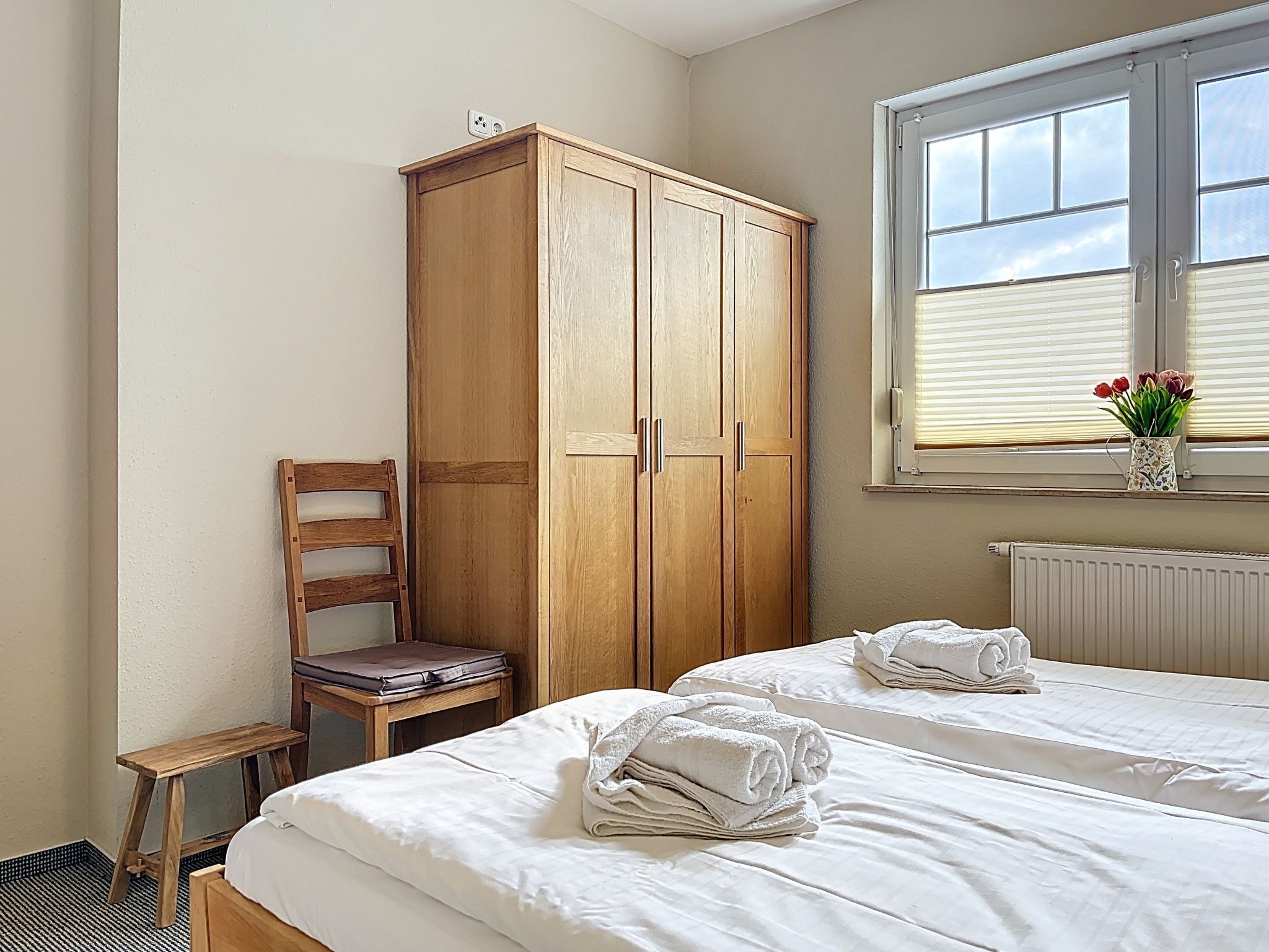 Une chambre avec deux lits, une armoire en bois, une chaise, une petite table et une fenêtre donnant sur un beau paysage.