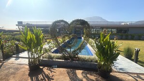 A pool surrounded by greenery, a building with a sign 'Monkey Hills Restaurant,' and a mountain in the background. - 7 Tree Resort & Restaurant (Paud)