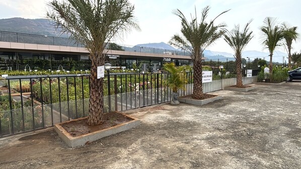 A parking area with palm trees, a fence, and a building with a sign for a nursery. - 7 Tree Resort & Restaurant (Paud)