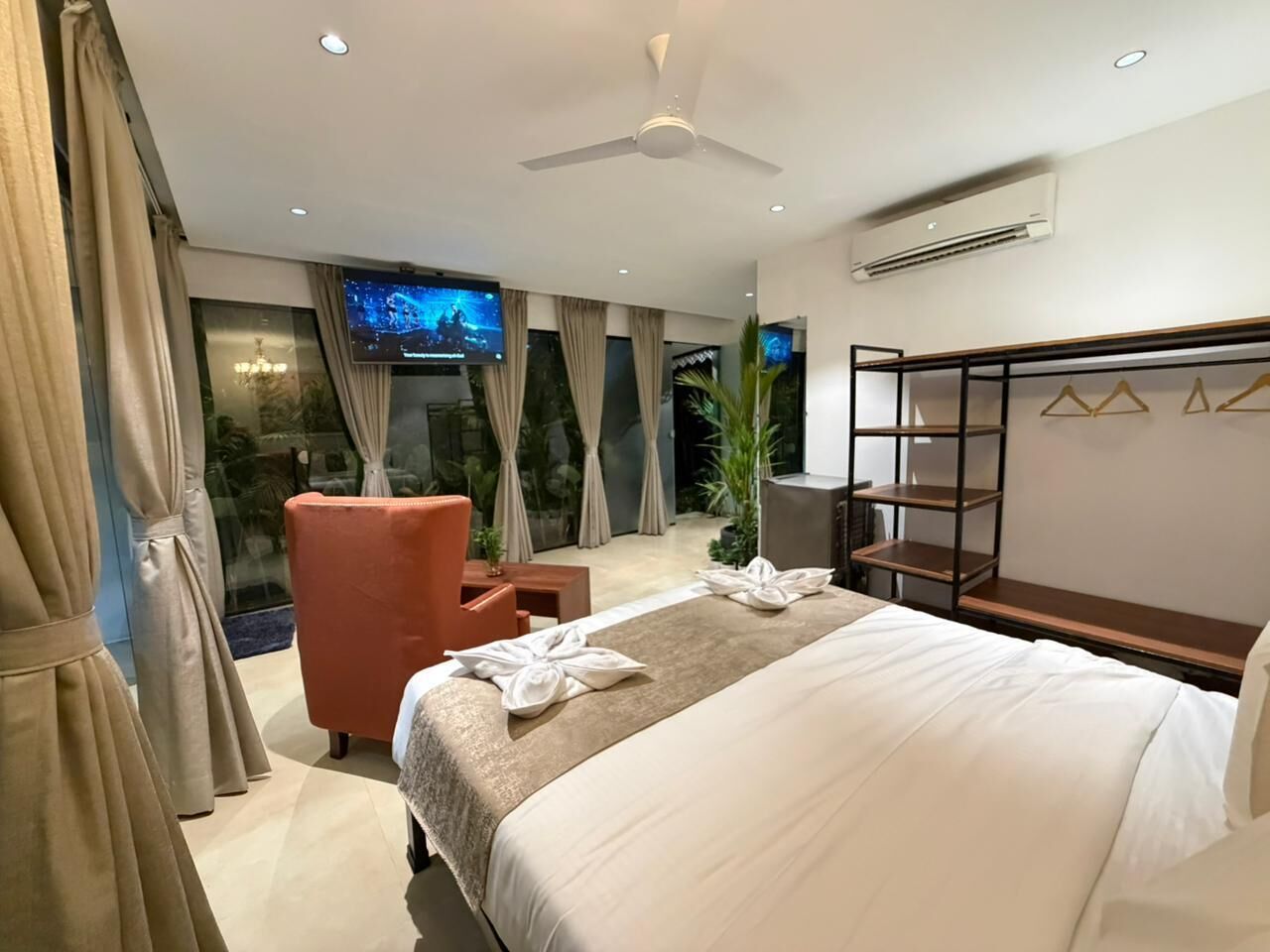 A hotel room with a bed, a TV, a chair, a desk, and a balcony with curtains.