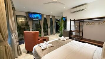 A hotel room with a bed, a TV, a chair, a desk, and a balcony with curtains.