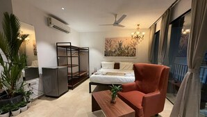 A modern hotel room with a bed, a red armchair, a wooden side table, a black shelving unit, and a large window with curtains. - 7 Tree Resort & Restaurant (Paud)