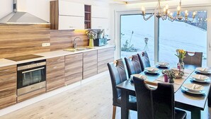 A modern kitchen with wooden cabinets, a built-in oven, and a dining area with a table and chairs. - Landhaus Bergkristall by Interhome (Dalaas)