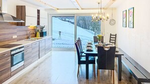 A modern kitchen with wooden cabinets, a built-in oven, and a large window overlooking a snowy landscape. - Landhaus Bergkristall by Interhome (Dalaas)