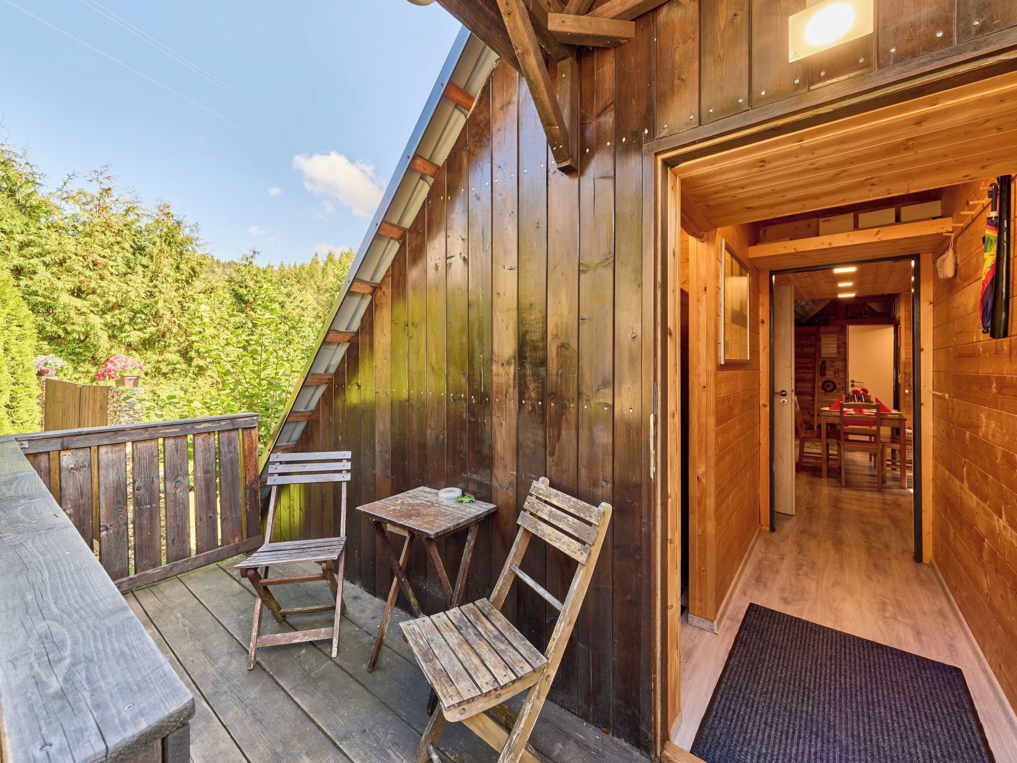 A wooden cabin with a balcony, two wooden chairs, and a table.