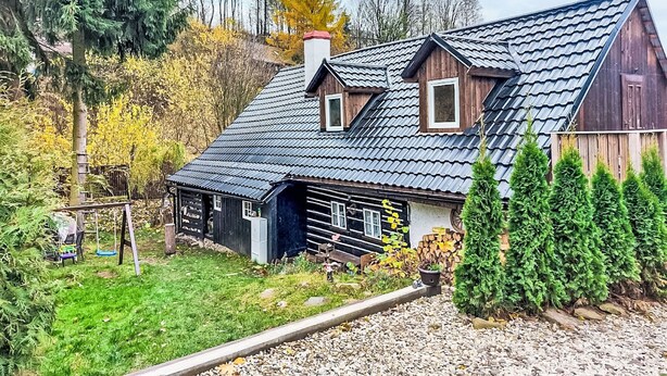 Una casa de madera tradicional con techo inclinado, un cobertizo pequeño adosado y un jardín bien cuidado con caminos de grava y vegetación.