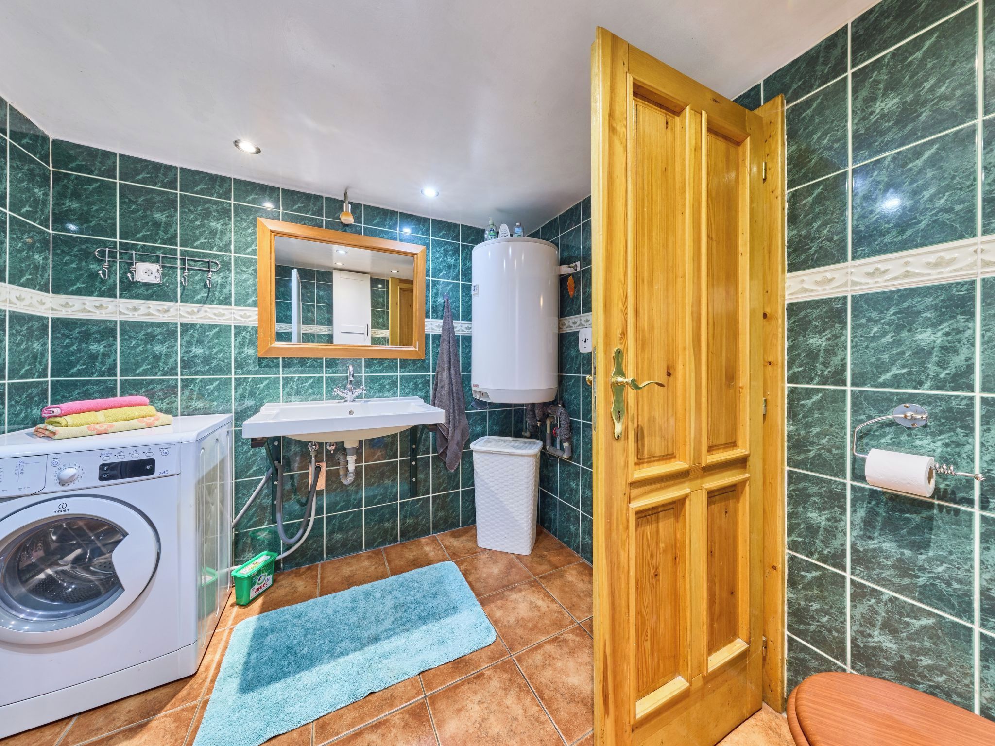 A compact bathroom with a washing machine, a sink, a mirror, and a toilet.