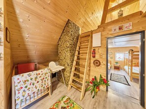 A cozy cabin interior with a wooden ceiling, a stone wall, a wooden ladder, a crib, a chair, and a door leading to another room. - Roubenka u potoka by Interhome (Výprachtice)