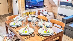 Un comedor con una mesa de madera dispuesta para seis personas, un televisor en la pared y una ventana con cortinas.