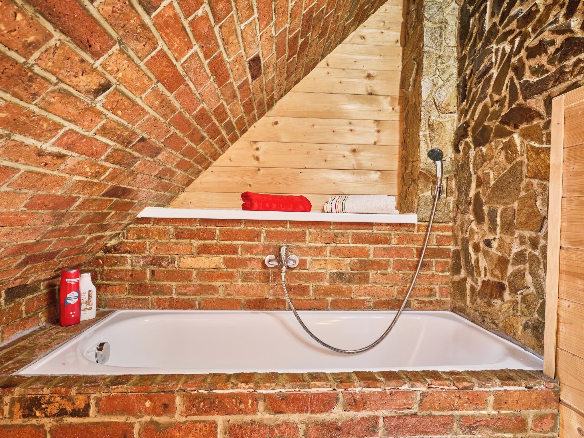 Ein Badezimmer mit Backsteinwand, Holzregal, einer Badewanne und einer Dusche.