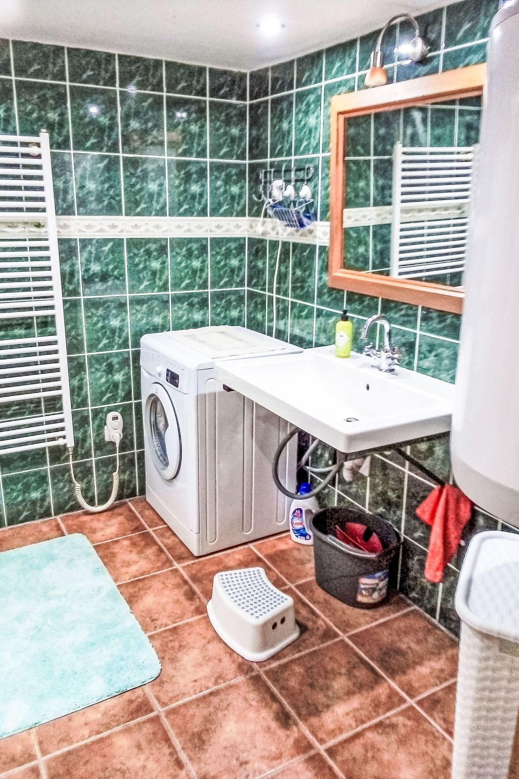Ein kleines Badezimmer mit Waschmaschine, Waschbecken, Spiegel, Handtuchhalter und kleinem Mülleimer.