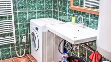 Ein kleines Badezimmer mit Waschmaschine, Waschbecken, Spiegel, Handtuchhalter und kleinem Mülleimer.
