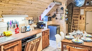 Un interior de madera con zona de cocina, mesa de comedor lista para una comida y una escalera que sube a un nivel superior.