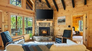 Een gezellig cabin interieur met een stenen open haard, houten wanden en een grote televisie aan de muur.