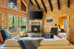 Interior acogedor de una cabaña con chimenea de piedra, paredes de madera y un televisor grande montado en la pared.