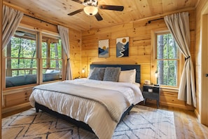 Une chambre dans une cabane en bois, avec un lit, des tables de chevet et deux fenêtres avec des rideaux.