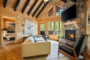 L’intérieur d’une cabane en rondins, avec une cheminée, un canapé, un fauteuil en cuir et un téléviseur fixé au mur.