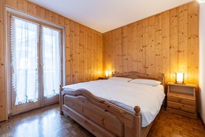 Ein Schlafzimmer mit Holzvertäfelung, einem Bett, zwei Nachttischen mit Lampen und einem Fenster mit Spitzenvorhängen.