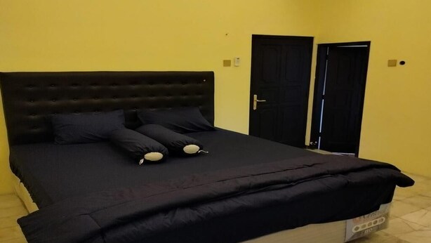 A single bed with a dark headboard, two black doors, and a yellow wall. - Cozzy Villa Garden Jogja  (Kalasan)
