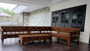 A traditional wooden bench and table set in a room with a tiled floor and a large window with dark frames. - Cozzy Villa Garden Jogja  (Kalasan)