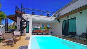 A modern house with a swimming pool, outdoor furniture, and a spiral staircase.