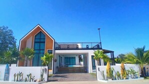 A modern two-story house with a large bay window, a balcony, and a pool.