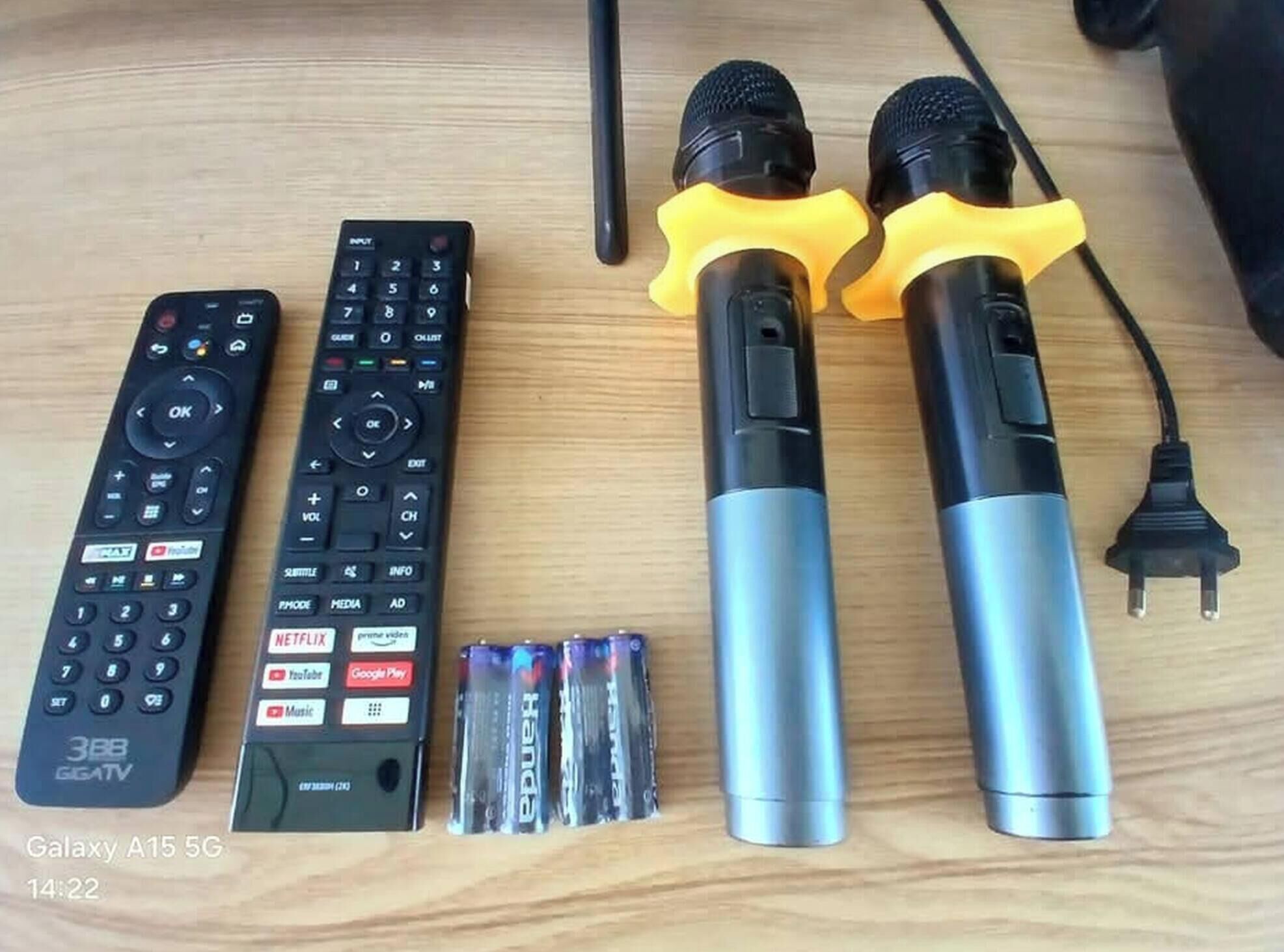 Deux microphones, une paire de télécommandes et un jeu de piles, le tout posé sur une surface en bois.