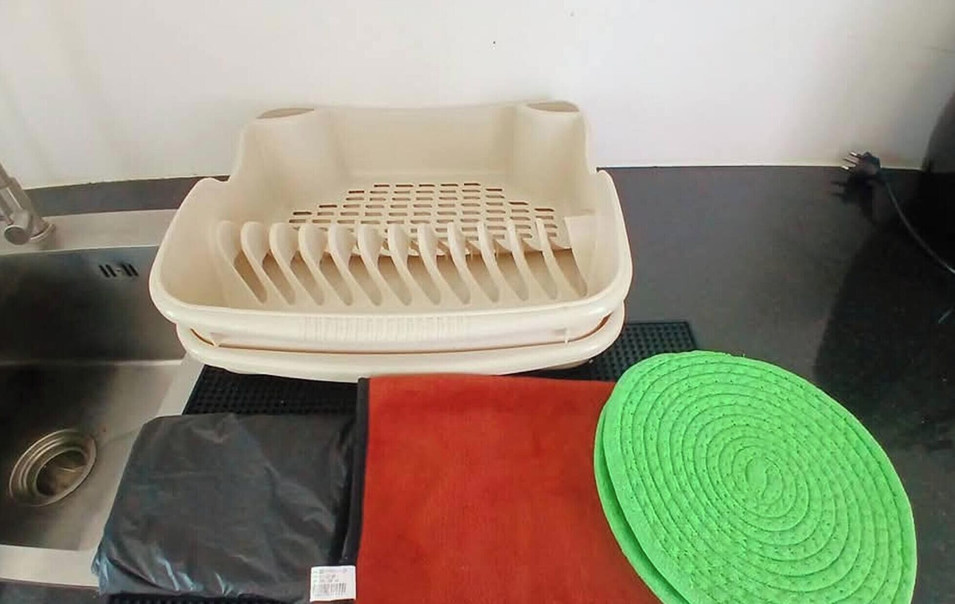 A kitchen area with a sink, a beige plastic tray, a black bag, a red cloth, and a green circular mat.