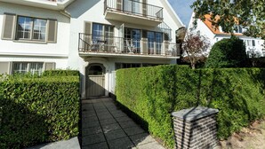 En bostadsbyggnad i två våningar med en balkong, en grind vid entrén och en välskött häck.