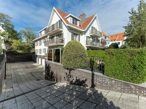 Ein zweigeschossiges Wohnhaus mit Ziegeldach und einem Balkon im zweiten Obergeschoss, im Vordergrund ein gepflegter Heckenstreifen.