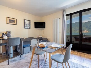 A modern room with a dining table, chairs, a sofa, a TV, and a view of the sea. - Leonard Lake by Interhome (Ghiffa)