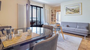 Ein modernes Wohnzimmer mit Essbereich, einer Couch, einem Bücherregal und einem Gemälde an der Wand.