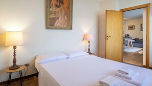Ein Hotelzimmer mit einem Bett, zwei Nachttischlampen, einem Bild an der Wand und einer Tür zu einem Essbereich.
