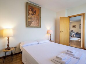 Ein Hotelzimmer mit einem Bett, zwei Nachttischlampen, einem Bild an der Wand und einer Tür zu einem Essbereich.