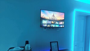 A room with a flat-screen TV displaying Disney movies, a coffee machine, and a table with a menu. - Room-private Master Bed & Bath #1 Cautle (Edmonton)