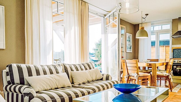 A modern living room with a striped sofa, a glass coffee table, and a dining area with wooden chairs. - Appartement in Zinnowitz mit Grill by Interhome (Zinnowitz)