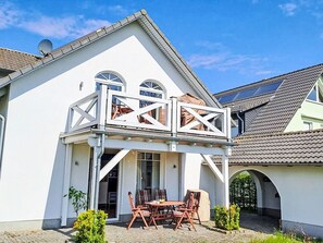 Une maison avec un balcon, un coin repas avec des chaises et une table, et un espace extérieur aménagé et abrité.