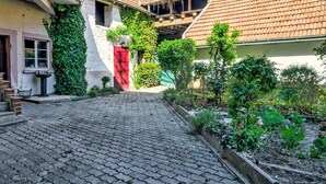 A cobblestone courtyard with a red door, a white wall with greenery, and a tiled roof. - Fewo Römerweg by Interhome (Neustadt an der Weinstraße)