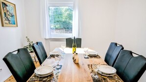 A dining room with a wooden table set for six, black leather chairs, a window with a view of greenery, and a painting on the wall. - Fewo Römerweg by Interhome (Neustadt an der Weinstraße)