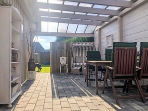 Ein überdachter Patio-Bereich mit Holzzaun, einem gestreiften Sofa und einem Tisch mit Stühlen.
