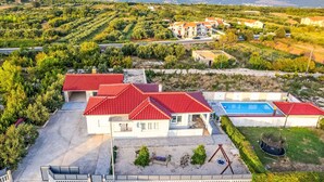 Ein Wohnhaus mit Swimmingpool, Gebäuden mit roten Dächern und Blick auf das Meer und die Berge.
