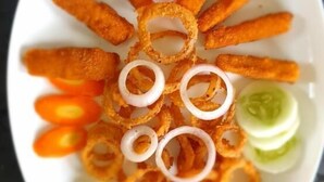 A plate of food with onion rings, pickles, and a small bowl of sauce. - Elephant Garden Hotel and Resort (Kanchanrup)